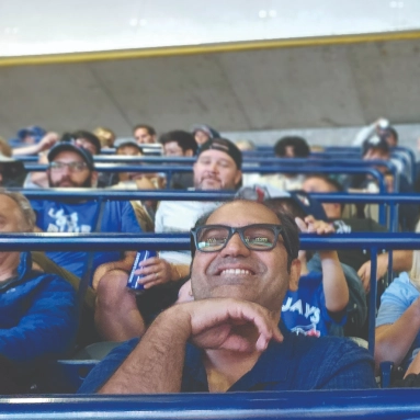 Smiling person in stadium seating with other fans in the background, looking toward the camera.