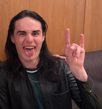 Person indoors making a “rock on” hand gesture and sticking out their tongue while smiling.