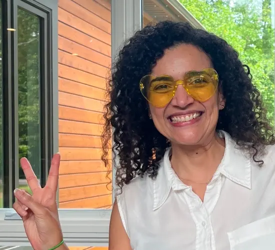 Smiling team member wearing yellow-tinted glasses and flashing a peace sign near a window.