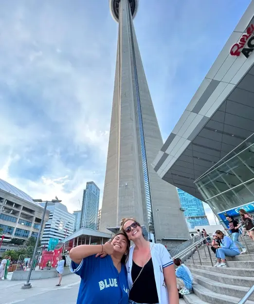 Two people smiling together outdoors with the CN Tower rising behind them.