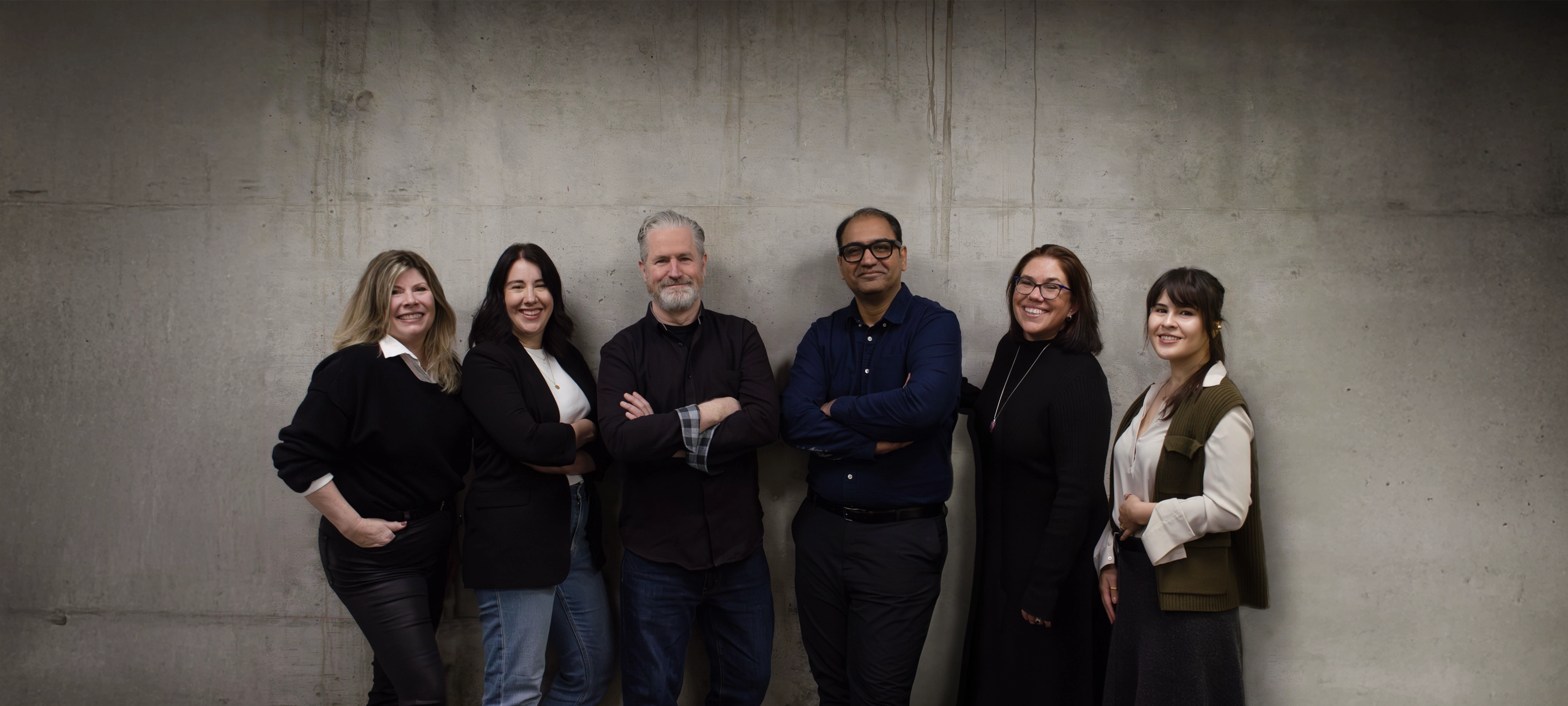 Context Creative leadership team of six standing side by side in front of a concrete wall.